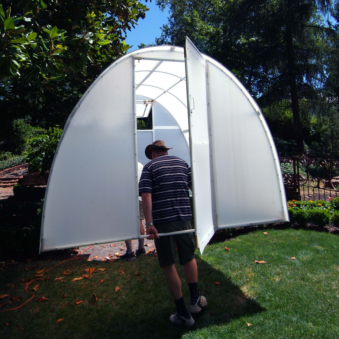 Two men installing early bloomer greenhouse in the garden