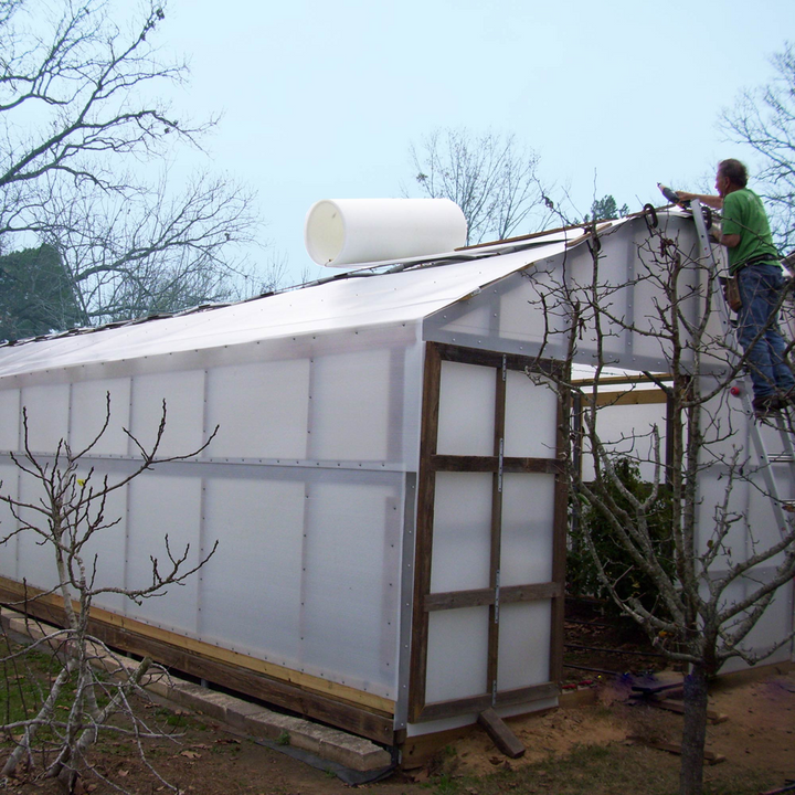 A man rolling Solexx Greenhouse Rolls on a outdoor greenhouse wood frame