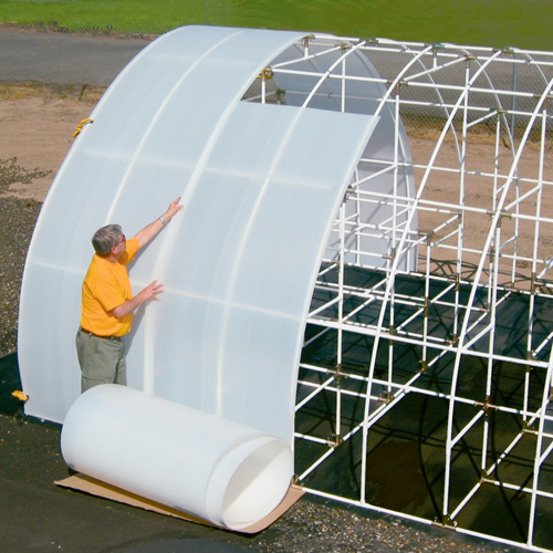 A man rolling Solexx Greenhouse Rolls on a outdoor greenhouse frame