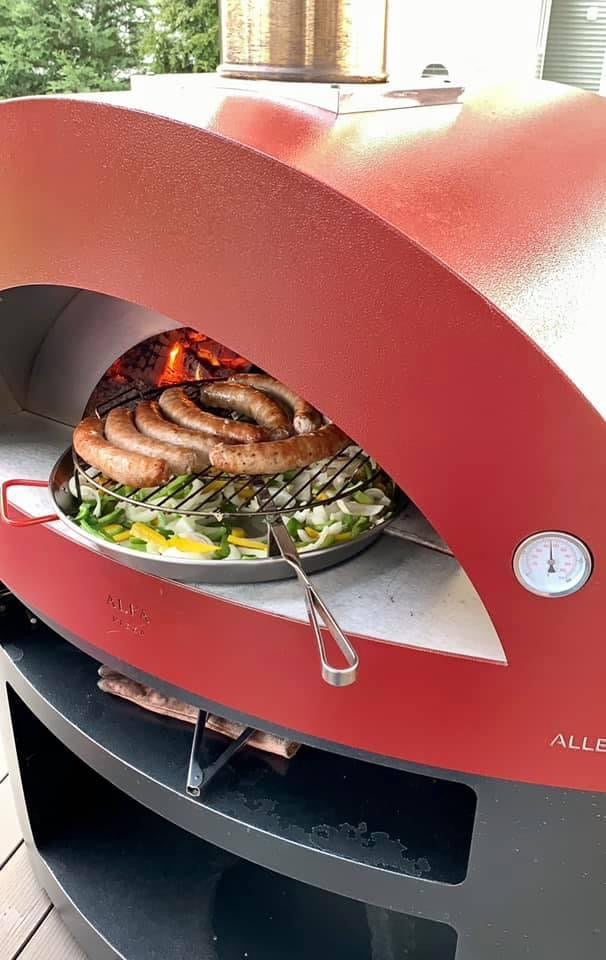 Alfa Allegro Wood Fire Pizza Oven Flames Raging and a Crafted Sausage and Vegetable Spread is prepared to be cooked 